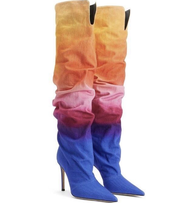 two kneehigh boots with stiletto heels are presented on a white background. the boots have a gradient or ombre effect, transitioning from yellow at the top, through orange, pink, and red, to blue at the bottom. they have a slouchy, gathered texture and appear to be made of fabric.