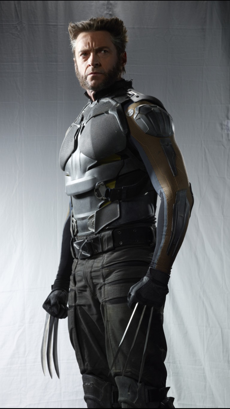 the image is a promotional shot of hugh jackman as wolverine, likely from an xmen movie. he is wearing a grey, armorlike costume with his signature metal claws extended from his gloves. he also has his iconic facial hair style. the background is plain, suggesting a studio setting.