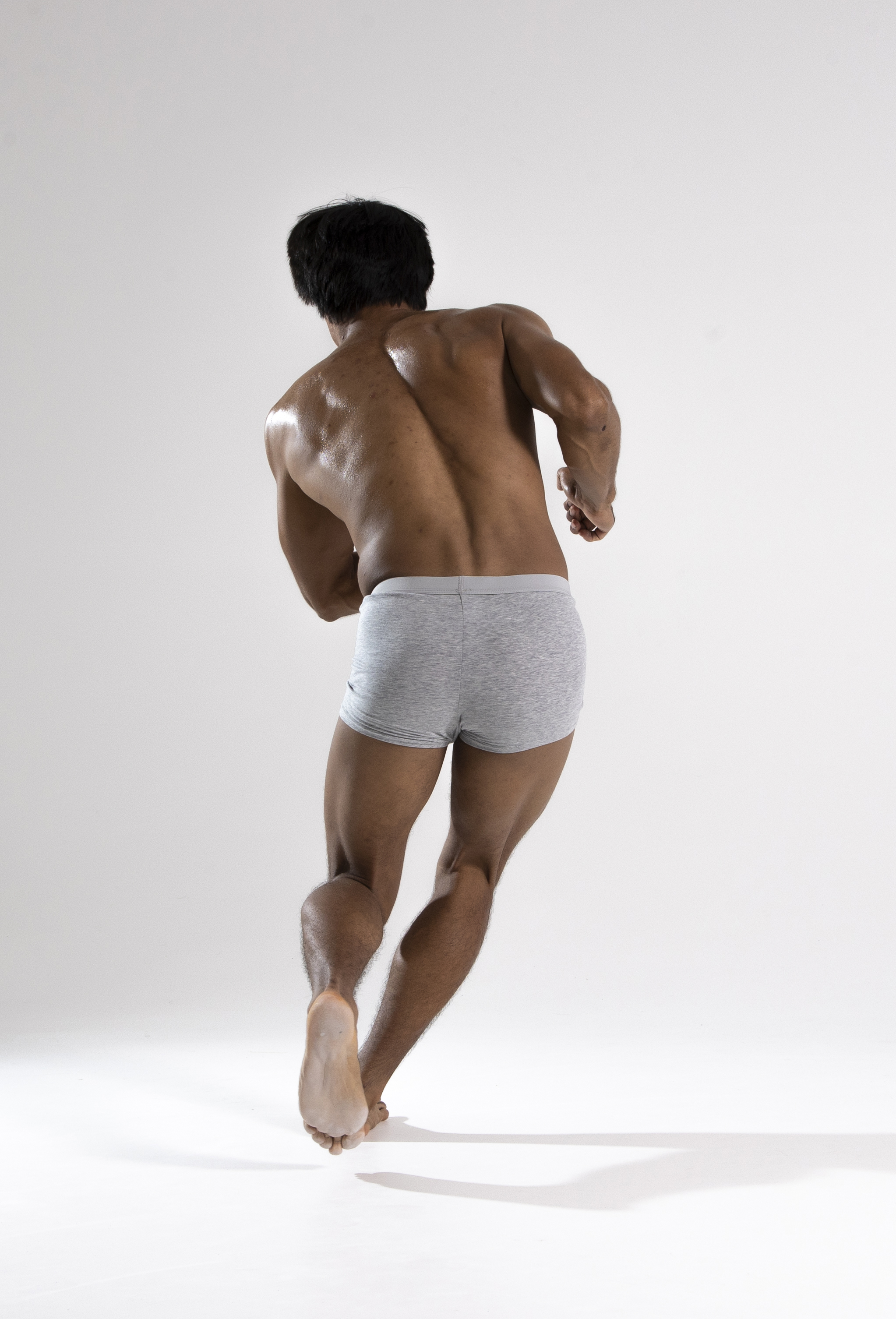 a photo of a muscular man running with his back to the camera, wearing gray underwear, against a white background.