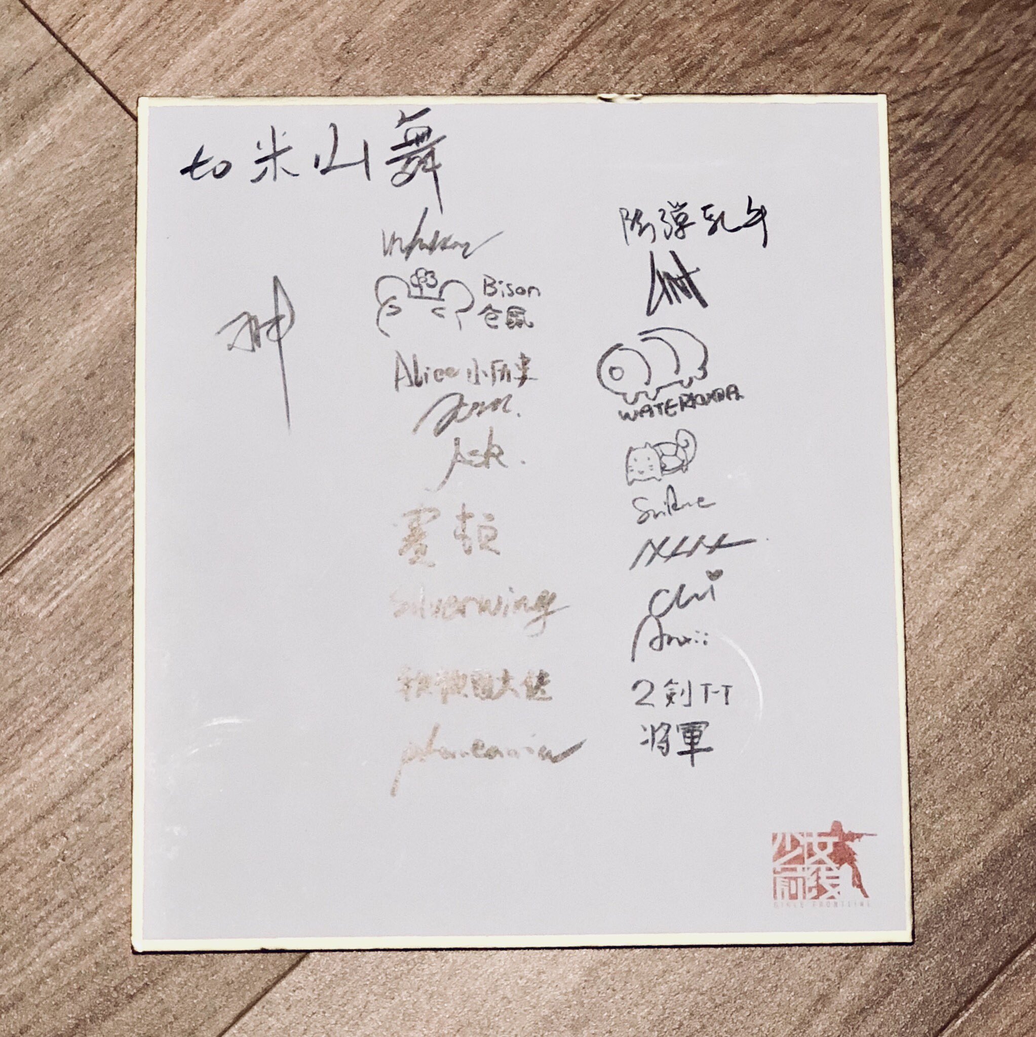 a white board with black and gray writing on it, along with some small drawings. the writing is mostly in japanese and appears to be a series of autographs and messages. there is a small red stamp in the bottom right corner.