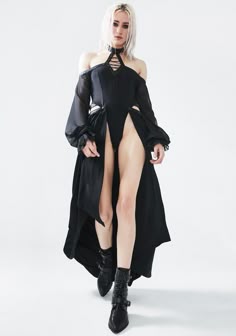 a woman wearing a black long sleeve dress and black boots poses in a studio. she is wearing her hair up.