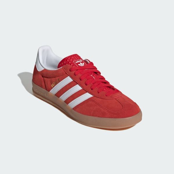 a pair of red adidas gazelle shoes with white stripes and a gum sole. the shoes are on a white background.