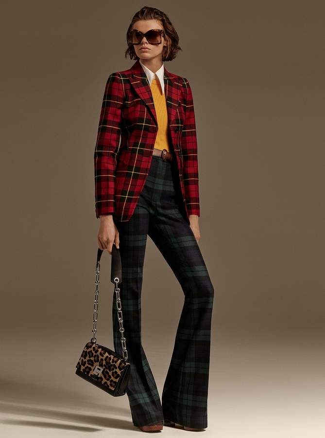 a woman wearing a red and black plaid blazer over a yellow top and a pair of black and green plaid bellbottom pants. she is also wearing stylish sunglasses and carrying a chain bag with a leopard print.