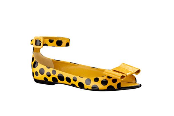 a yellow open toe flat women's shoe with black polka dots and an ankle strap is set against a white background. there is a yellow bow on the top of the shoe.
