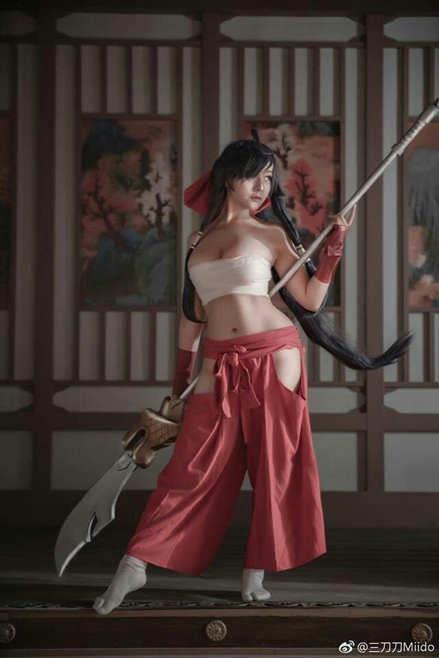 a woman in a cosplay costume is holding a spearlike weapon. she is wearing a white strapless top and red pants with cutouts. she is barefoot, wearing lightcolored socks. the background suggests a traditional asian setting with wooden screens and painted panels.