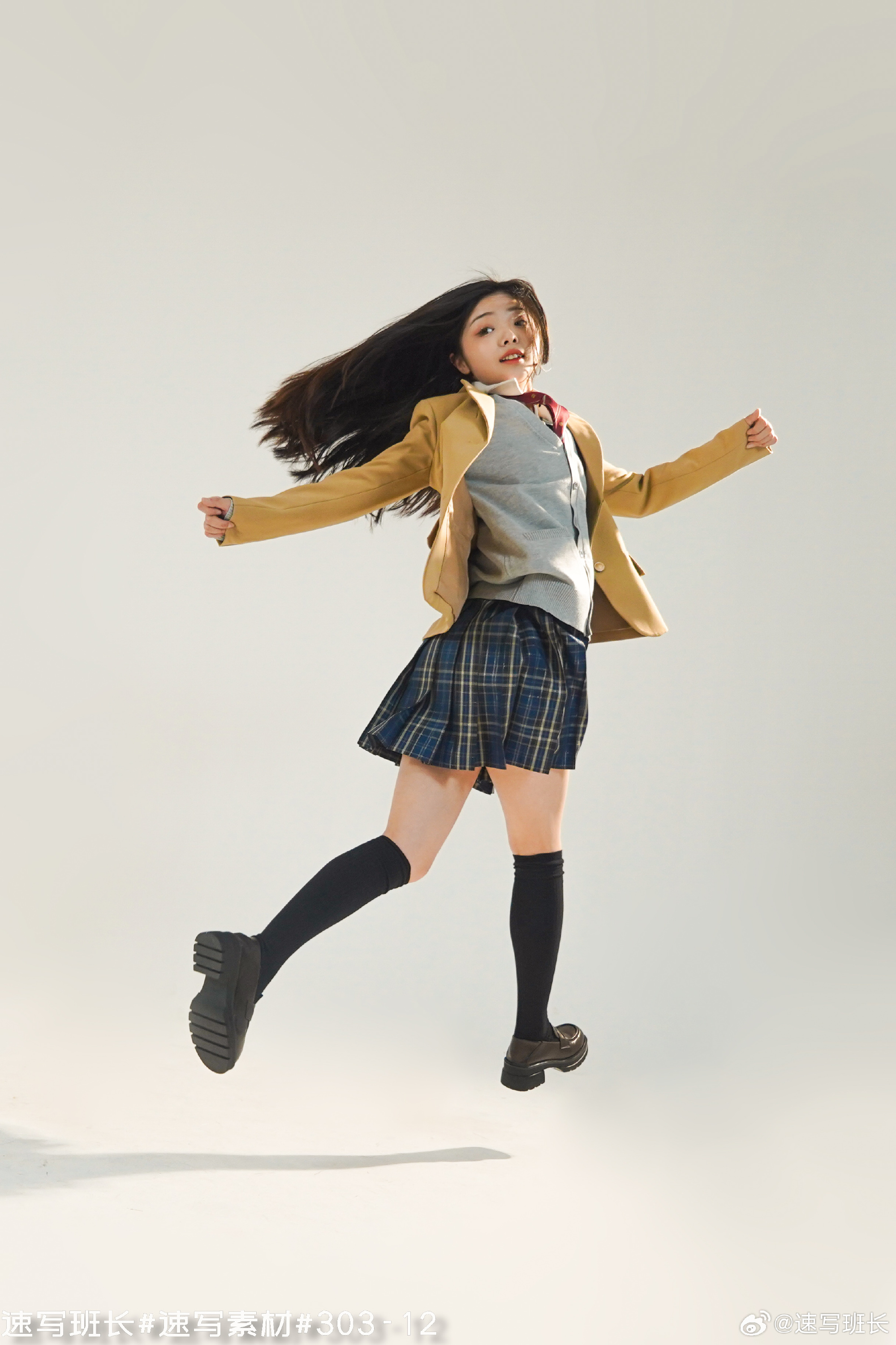 a young woman in a yellow blazer, grey sweater vest, plaid skirt, and black kneehigh socks leaps in the air against a plain white background. her long black hair flows behind her, and her expression is joyful. the lighting is soft and natural, suggesting a studio setting. the low camera angle emphasizes her height and the energy of her jump.