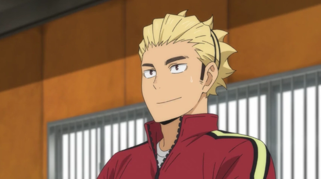 a smiling bokuto koutarou from haikyuu is shown from the chest up, turned slightly to the left, and looking at something to the left of the viewer. he is wearing a red athletic jacket with yellow stripes on the sleeves over a white shirt. he has spiky, light blonde hair with black streaks. the background is blurry, but it appears to be a gymnasium with tan walls and a window with white bars on the right side.