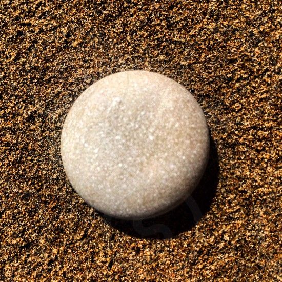 a single round, smooth, white stone sits on a bed of brown sand. the stone is in focus while the sand is blurred in the background. the stone appears to be a pebble.