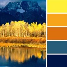 the image is a landscape photograph of a mountain range with fall foliage in the foreground. the trees are yellow and orange, and the mountains are blue and white. there is a lake in the foreground, and the reflection of the mountains and trees is visible in the water. the sky is blue and sunny.