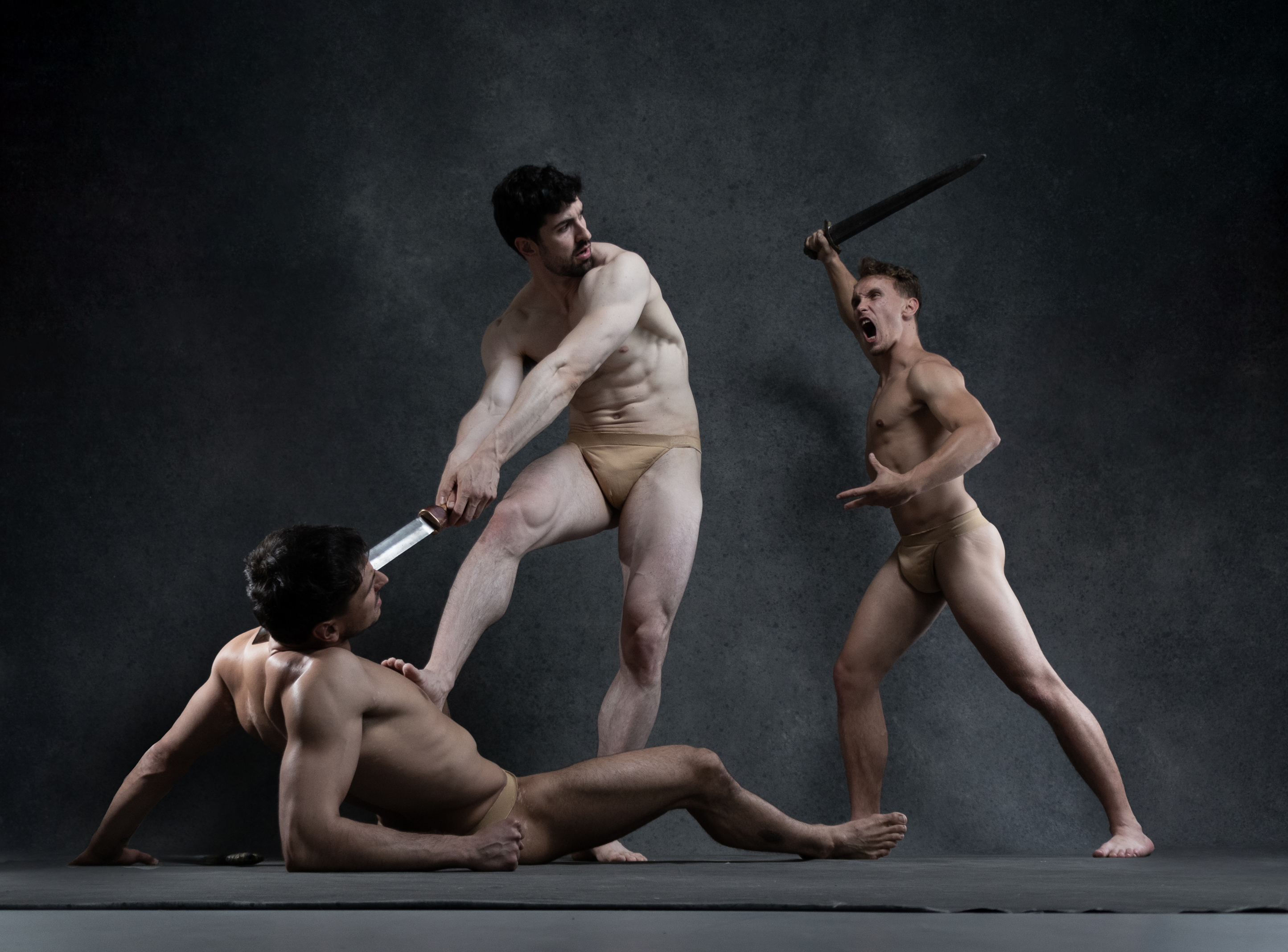 three nude men are engaged in a dynamic and dramatic struggle. the background is a dark gray, and the lighting is dramatic, highlighting the men's musculature. the man on the left is on the ground, while the other two are standing. the man in the center is holding a sword, and the man on the right appears to be defending himself.