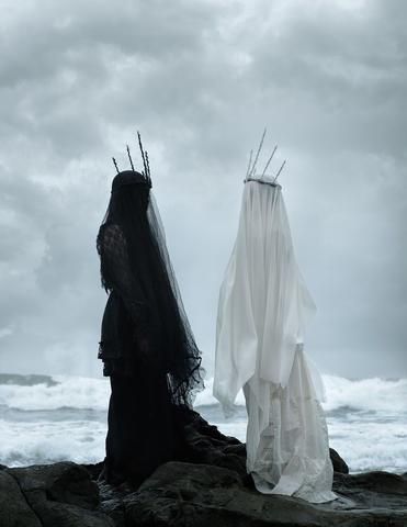 the image features two women, dressed in contrasting black and white, standing against a dramatic backdrop of a cloudy sky and stormy ocean waves. they wear flowing veils that enhance their ethereal and mysterious presence. the blackclad woman stands on the left, shrouded in darkness, while the whiteclad woman stands on the right, radiating light. the juxtaposition of black and white creates a striking contrast, highlighting the difference in their characters. the image conveys a sense of mystery and intrigue, leaving the viewer to wonder about their stories and the reason for their presence in this desolate landscape.