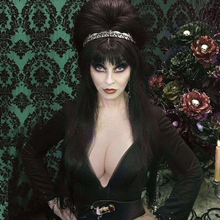 a woman with long, black hair, wearing a lowcut black dress and a black headband, looks at the camera with a dark and alluring expression. the image is dark and mysterious, with a gothic feel.