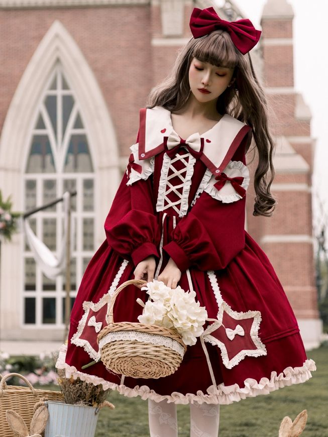 a young woman wearing a red and white lolita fashion dress stands outside a church. she is holding a wicker basket with white flowers in it and has a red bow in her hair. the dress has a square neckline, long sleeves, and a full skirt with lace trim. the dress is decorated with bows and ribbons.