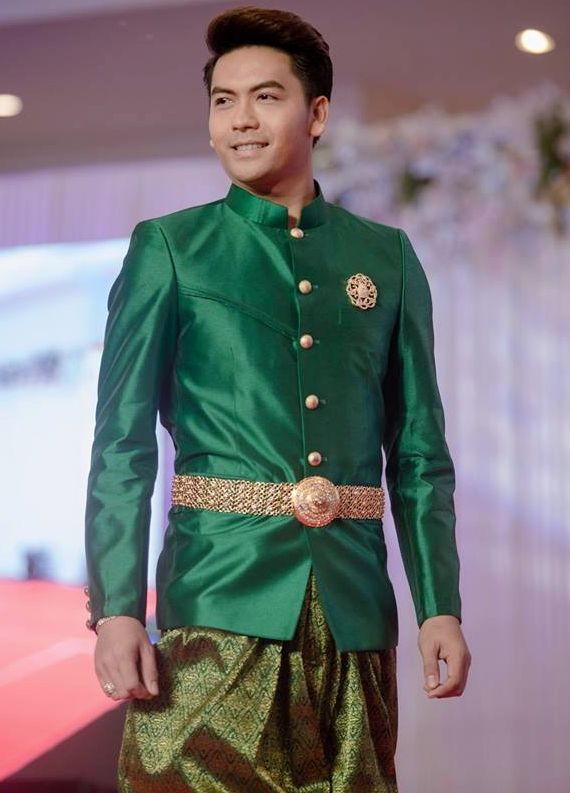 a young man in a traditional thai outfit, a green jacket and matching pants with gold accents. the man is smiling and looking to the side. he is dressed up for a special occasion like a wedding.