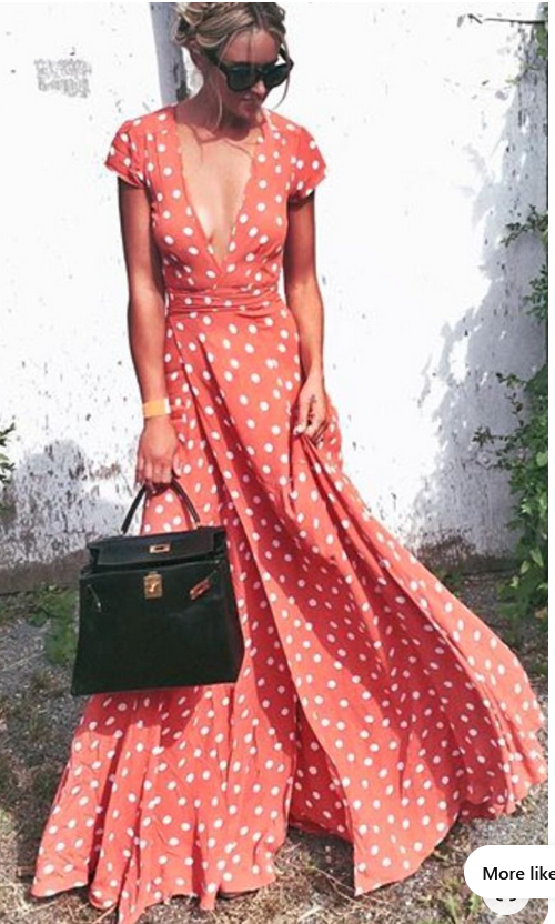 a woman in an orange and white polka dot dress stands outdoors on a sunny day. she is wearing sunglasses and carrying a black handbag. the dress is flowing in the wind.