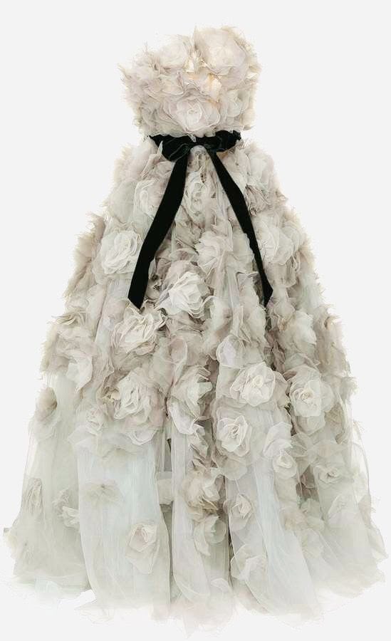 a strapless, light grey gown adorned with many fabric roses, accented with a wide black velvet ribbon tied at the bodice. the dress appears to be made of tulle, giving it a light and airy feel, and is couture.