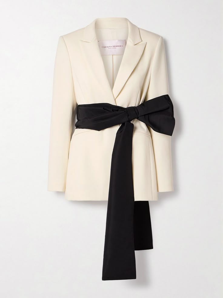 a creamcolored carolina herrera blazer with a large black bow tied at the waist. the blazer is on a white background.