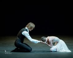 a male and female ballet dancer perform a graceful and emotional routine on stage. the male dancer is dressed in a black suit and the female dancer is wearing a flowing white dress. they are both in midpose, their bodies contorted in a beautiful display of artistry and athleticism. the lighting on the stage is dramatic, highlighting the dancers' movements and expressions.