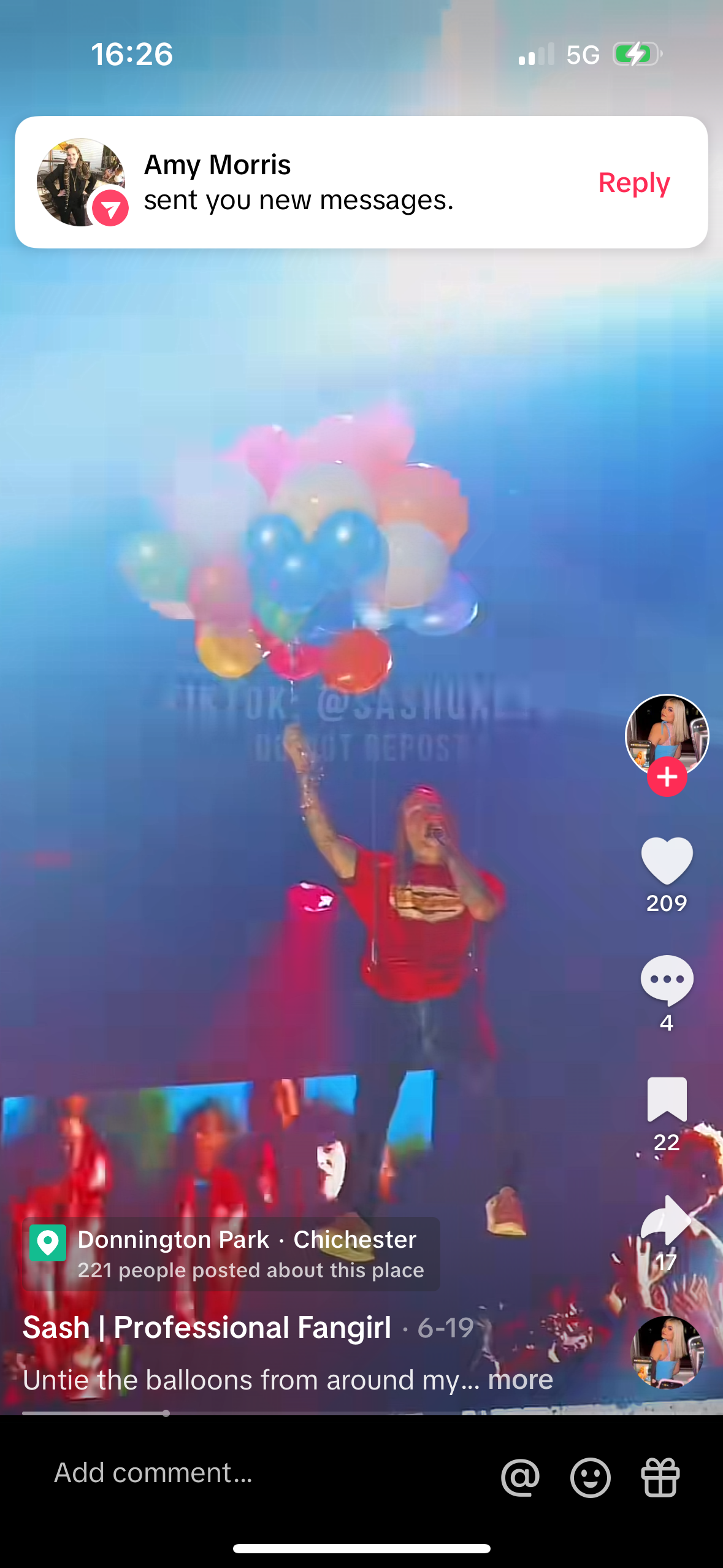 this is a screenshot of a tiktok video playing on a smartphone. the video is of a woman with red hair who is standing in a crowd of people holding a bunch of balloons. she is dancing and smiling. the video is captioned "untie the balloons from around my...."  and has a comment section below. the top of the screen shows a notification from amy morris.  the bottom right of the screen shows a heart icon and the number 209, which represents the number of likes.  the bottom left of the screen shows a location pin and the name donnington park, chichester.