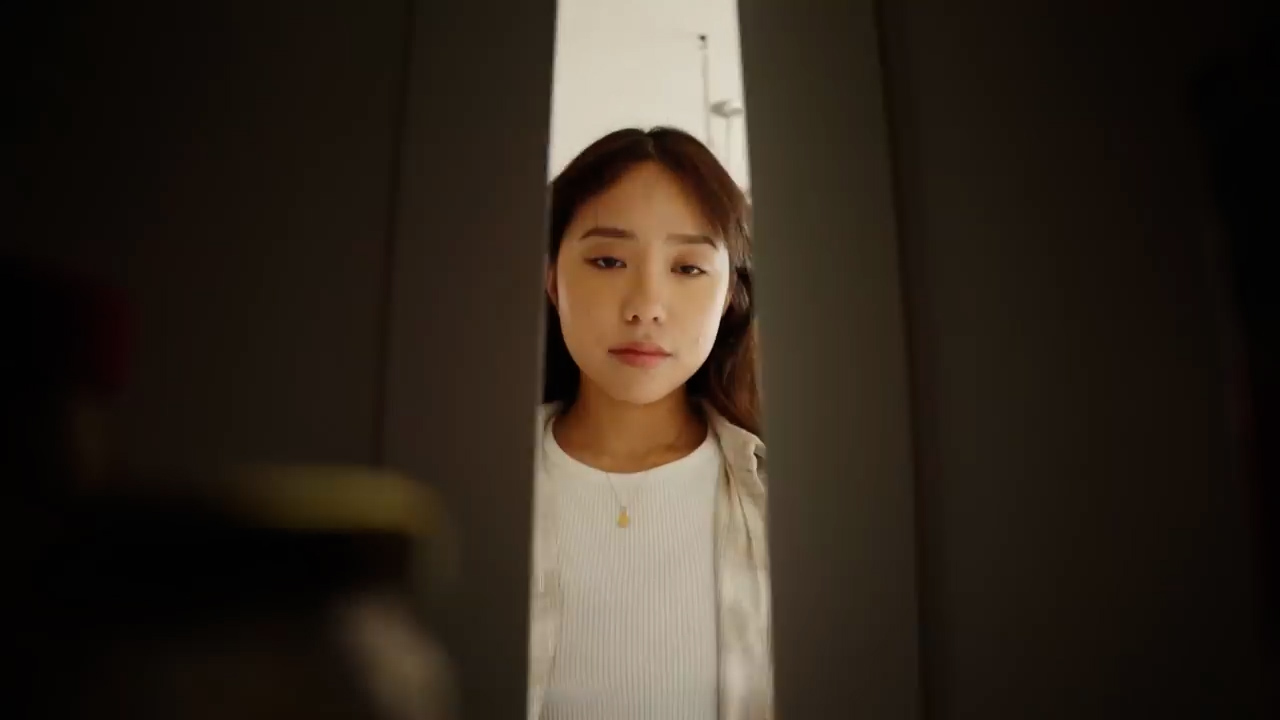 a young woman with long dark hair peeks inside her refrigerator, her expression neutral as she surveys its contents. the image is taken from inside the fridge, offering a unique perspective through the open door. the warm, slightly dim lighting adds to the relatable scene of someone searching for a snack or meal.