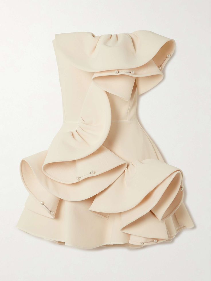 a closeup shot of a beautiful white ruffled dress with pearl embellishments. the dress is off the shoulder and has a mini length. it is a beautiful and feminine dress that would be perfect for a special occasion.