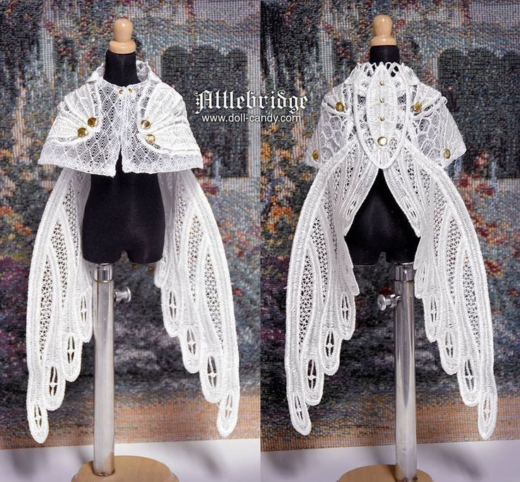 two images sidebyside show the front and back views of a white lace cape with gold buttons displayed on a black doll mannequin. the cape has intricate lace details resembling fairy wings. it is presented on a display stand in what appears to be a studio setting. the "littlebridge" logo and website address "www.dollcandy.com" are visible in the middle.