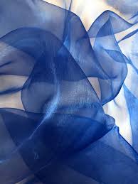 a closeup image of a blue, semisheer organza fabric. the fabric is draped and folded, showcasing its translucency and light, airy texture. the deep blue color creates a sense of richness and elegance.content: fabric, textilepeople: noneenvironment: indoorlighting: soft, diffusedperspective: closeupkw: blue, organza, sheer, fabric, textile, drape, folds, texture, translucent, elegant, rich.