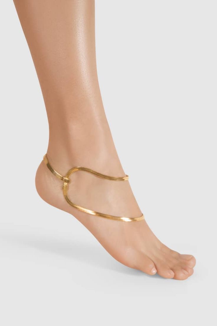 a woman's foot wearing a gold ankle bracelet. the bracelet is a thin chain that wraps around the ankle twice. the woman's foot is bare and the background is white.