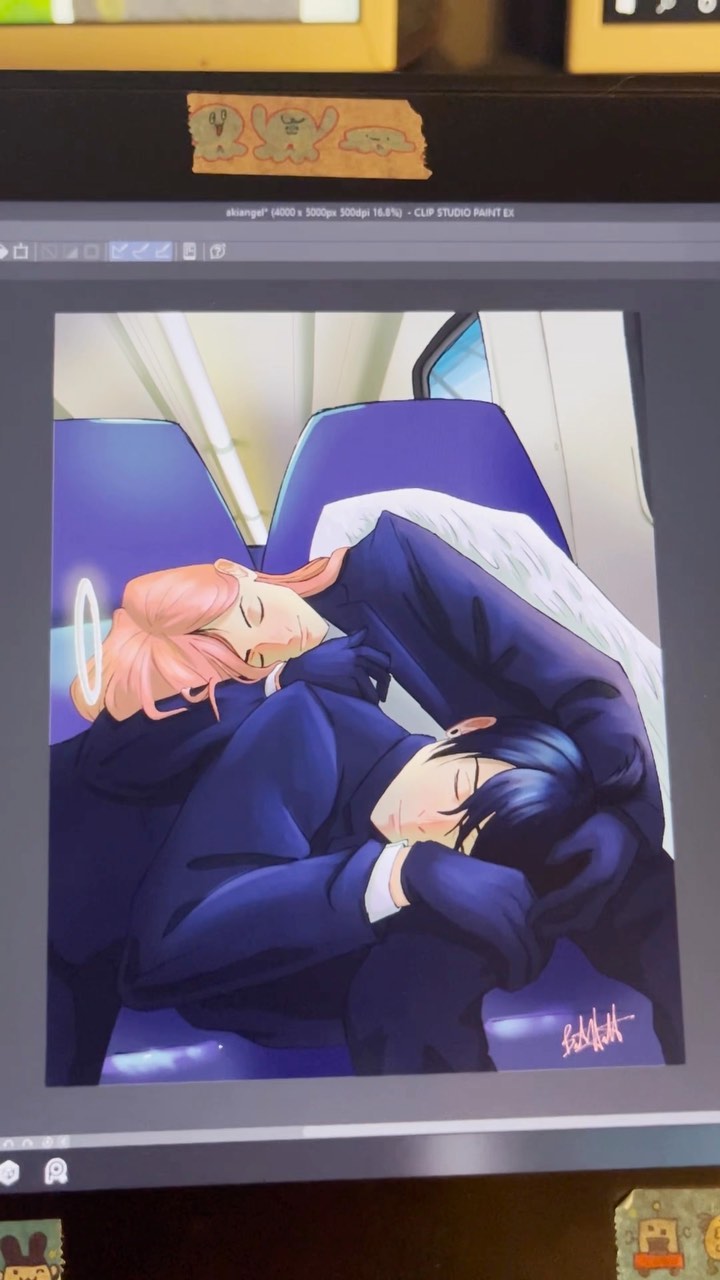 closeup shot of a computer screen displaying digital fanart. the artwork depicts an animestyle couple, a woman with light pink hair and a man with dark blue hair, asleep nestled together on a train seat.  the woman has a small halo above her head. they are dressed in dark blue suits and the woman's hand rests gently on the man's shoulder. the background suggests a train car with purple seats. the artwork style is soft and romantic. the image also shows a portion of the computer desktop, including file information indicating it was created in clip studio paint.  there are small stickers or decorative elements visible at the top and bottom of the computer screen.