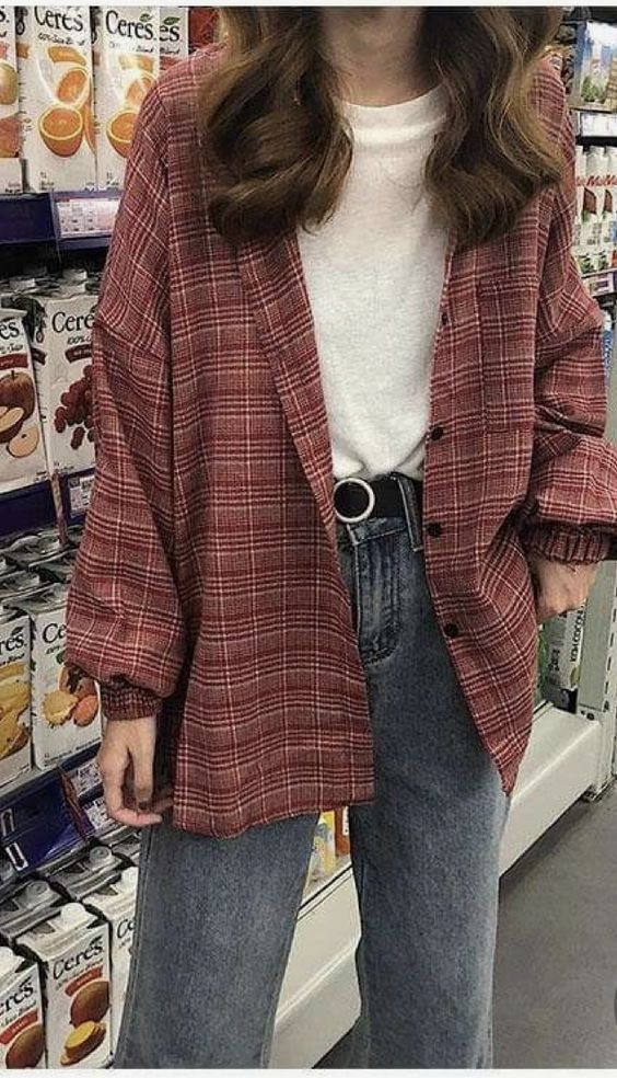 a woman in a red plaid shirt, white tee and blue jeans poses in a grocery store aisle.  she has long dark brown hair and is wearing a silver belt.  she is looking at the camera.