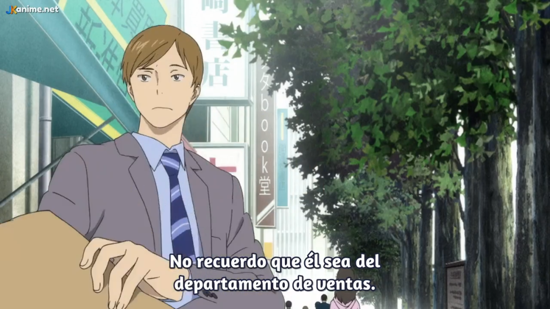 a screenshot from an anime featuring a young man with brown hair wearing a gray suit and blue tie. he is sitting outside on what appears to be a bench, with a city street lined with trees and buildings visible behind him. the lighting suggests a slightly overcast daytime setting. the man has a contemplative expression on his face. the bottom of the image contains spanish text that translates to "i don't remember him being from the sales department."