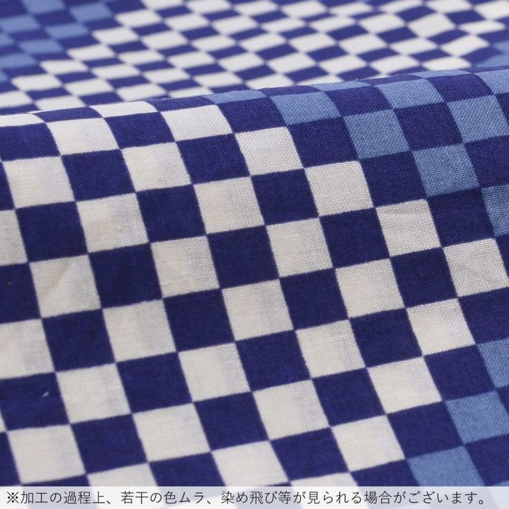 a closeup shot of a textile fabric with a blue and white checkerboard pattern. the fabric has a slight texture, and the blue squares appear in various shades. the pattern is consistent across the image. the bottom has a short japanese text line.