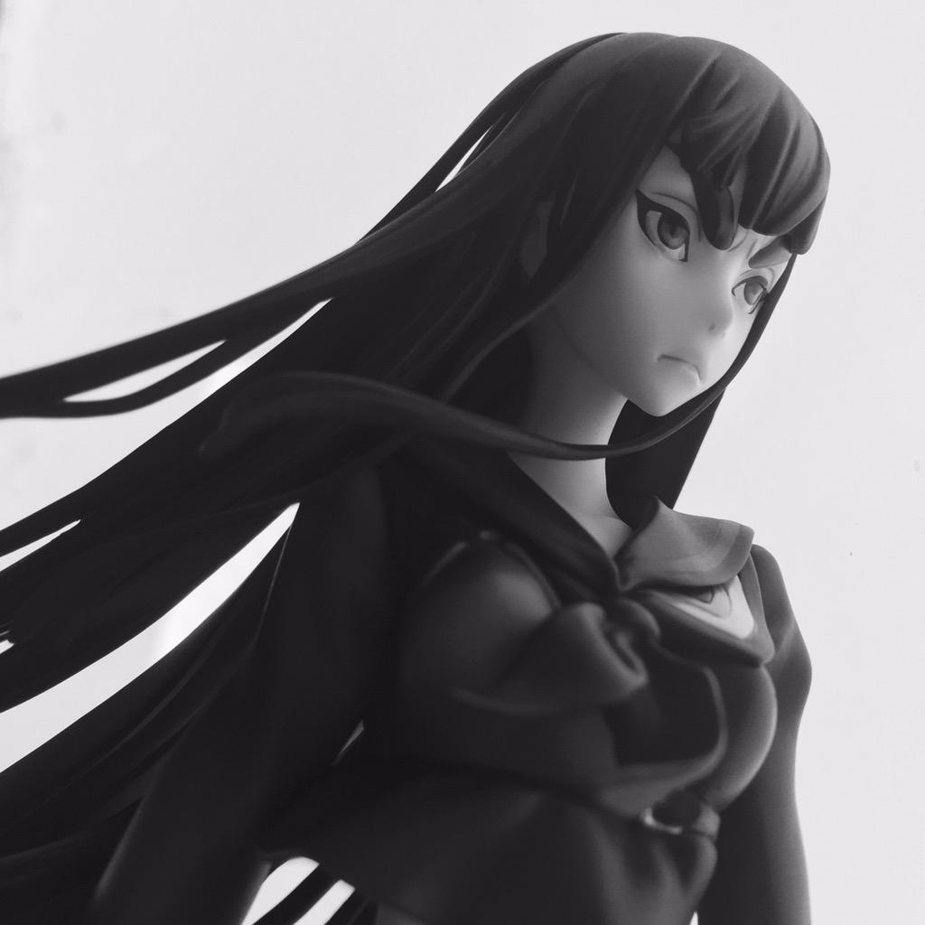 a black and white image of an anime figurine with long black hair. the figurine is wearing a school uniform and has a serious expression.