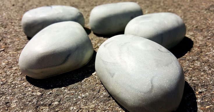 five smooth, gray, oval stones lay on a rough surface, close up.  the stones are rounded and smooth, with a white veining, giving them a marblelike look.  they are lit with soft lighting.