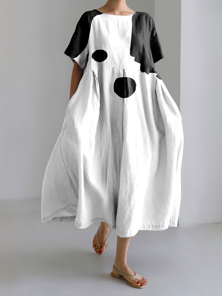 a woman in a white and black dress stands in front of a plain white wall. she has her hair pulled back. she is wearing a simple black and white dress with a doglike graphic on the front. she is wearing simple nude sandals. she is looking off to the side and smiling slightly. she is wearing no jewelry.