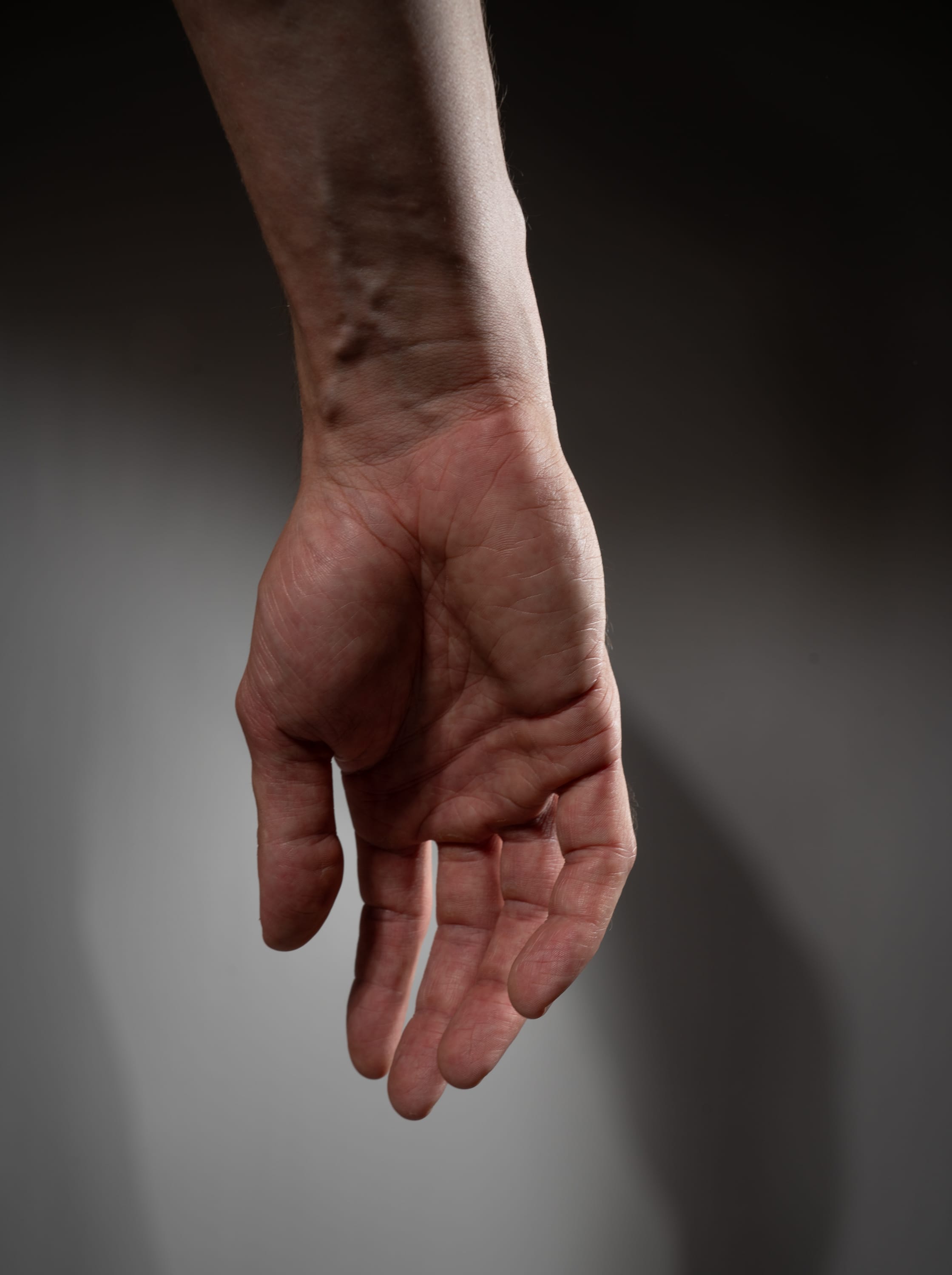 a man's hand is extended downwards, with the palm facing the viewer. the hand shows visible veins and has a natural skin tone. the image is taken against a neutral gray background.