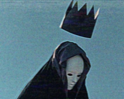 a man with a black crown on top of his head is wearing a black hooded robe. the man is wearing a white mask and is looking down with a solemn expression.  the background is a blue, textured wall.  the figure appears to be standing in the shadows.