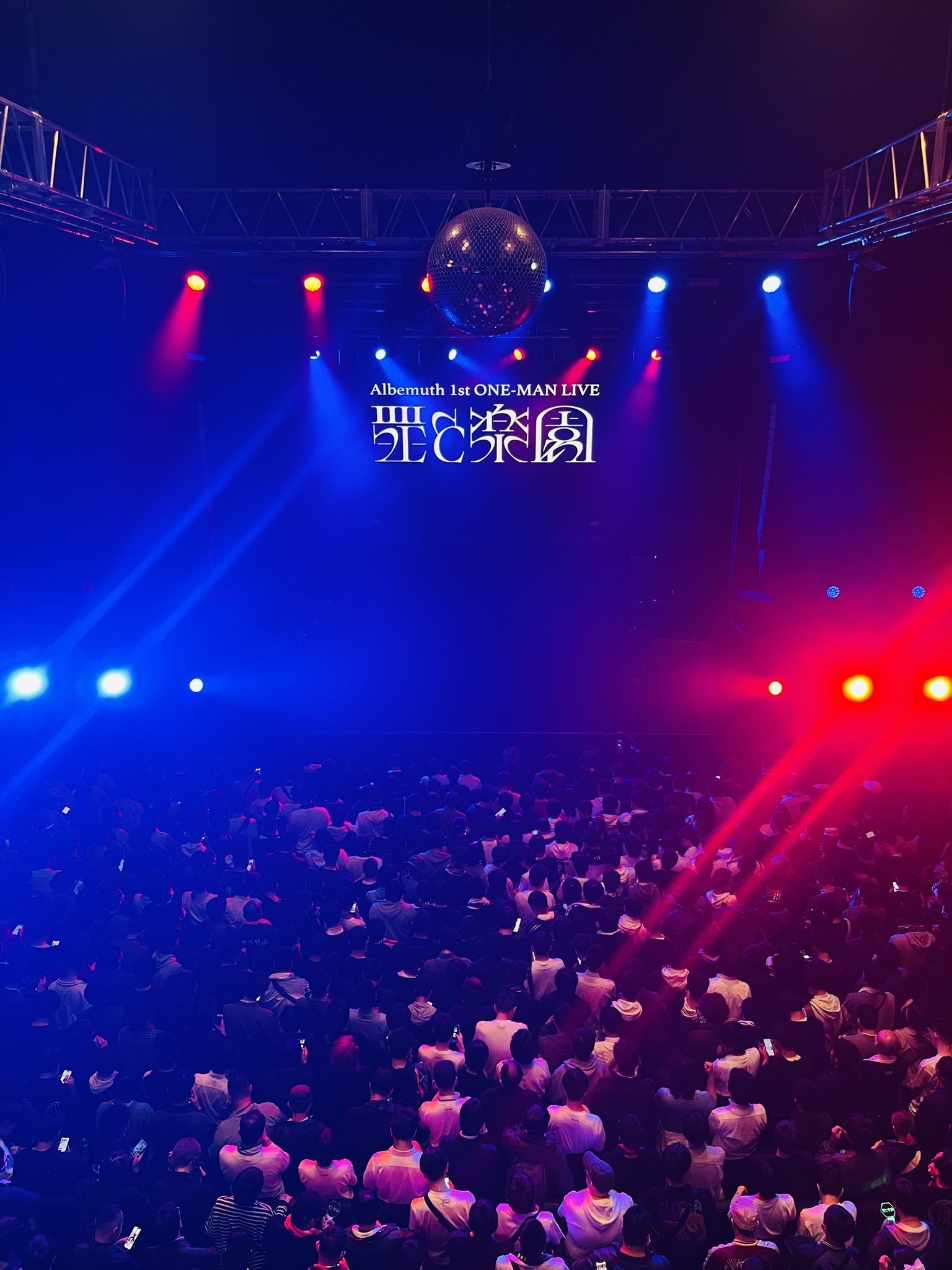 a poster for aftermath's 1st oneman live concert. the image shows a crowd of people at a concert, looking up at the stage. the stage is lit up with colorful spotlights and the crowd is holding up their phones. the poster is in japanese and english.