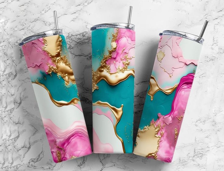 three stainless steel tumblers with a marble design of pink, teal, and gold colors are arranged on a white marble surface. the tumblers have stainless steel straws inserted, and the design incorporates swirling patterns and metallic accents.