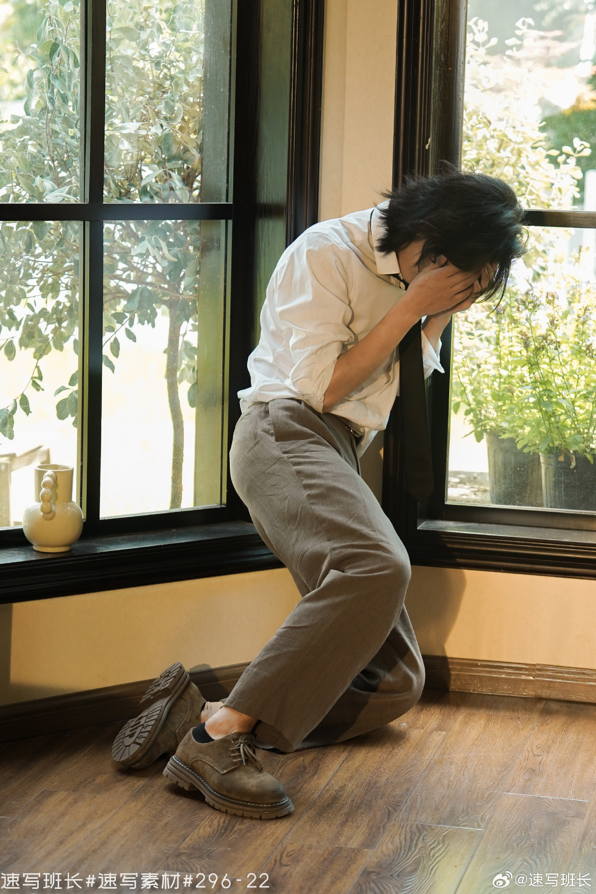 a man is kneeling on the floor with his hands covering his face. he appears to be distraught and possibly crying. the photo is taken from an eyelevel perspective. the environment is indoors, and natural light is streaming in from a window to the left of the man. the top five colors are light brown, offwhite, dark brown, tan, and dark gray.