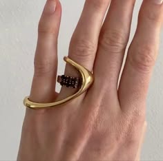 a hand with a gold ring on the middle finger. the ring is a large, abstract shape with a smaller ring on the index finger. the hand is against a white background.
