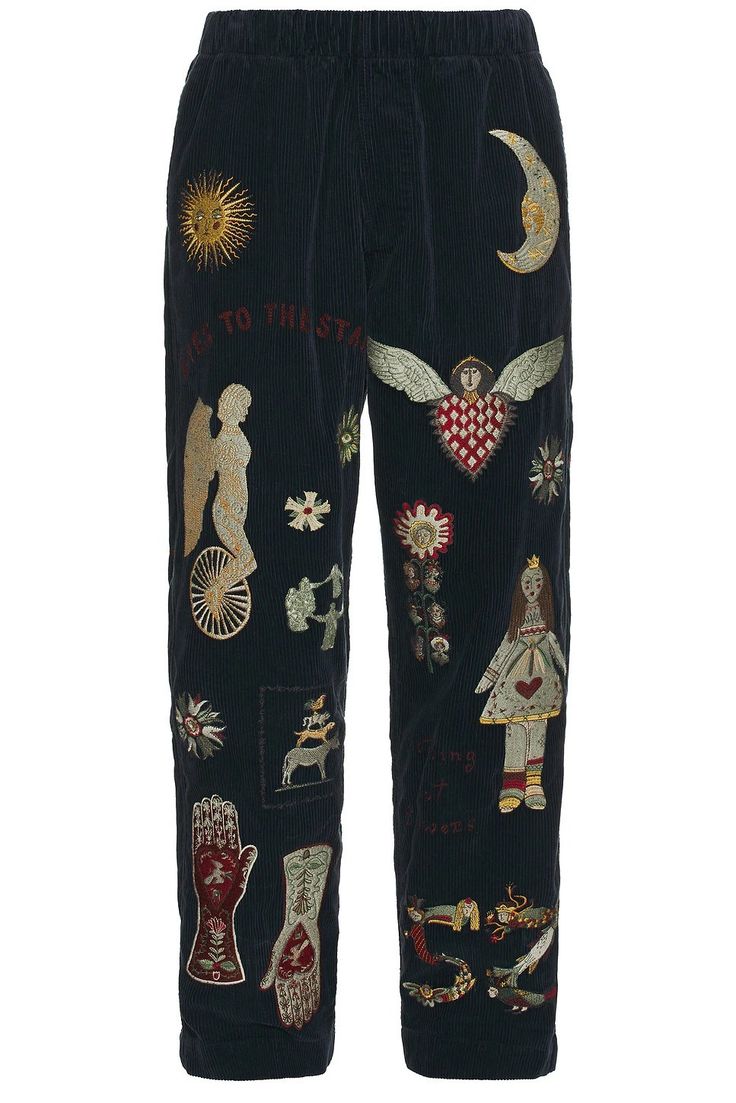 the image shows a pair of dark blue corduroy pants with various embellishments. the embellishments include a sun, a moon, a winged heart, an angel on a wheel, a doll, and two hands. the embellishments appear to be embroidered.