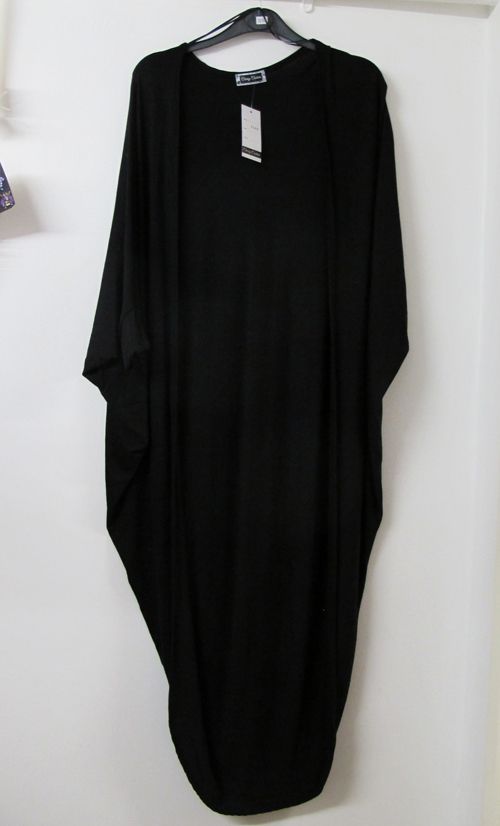 a black kimono is hanging on a hanger in front of a white wall. the kimono has long sleeves and falls to about ankle length. a white tag is attached to the garment.
