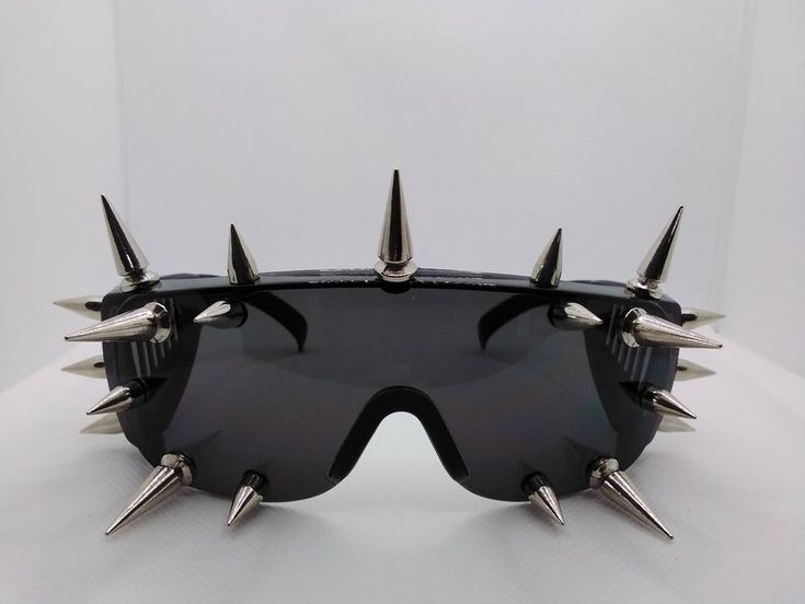 a pair of black punk sunglasses with silver spikes around the frames. the sunglasses are lying on a white surface.