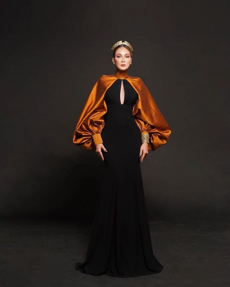 a woman stands in a fullbody portrait, wearing a black gown with a bronze cape and a crown, exuding an elegant and queenlike presence.