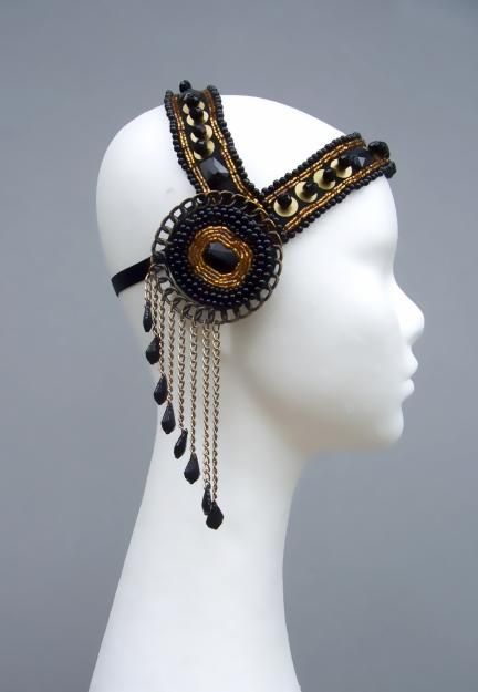 a close up of a black and gold headpiece on a white mannequin head. the headpiece is made of black and gold beads and chains. it is a beautiful and ornate piece of jewelry that would make a statement at any event.
