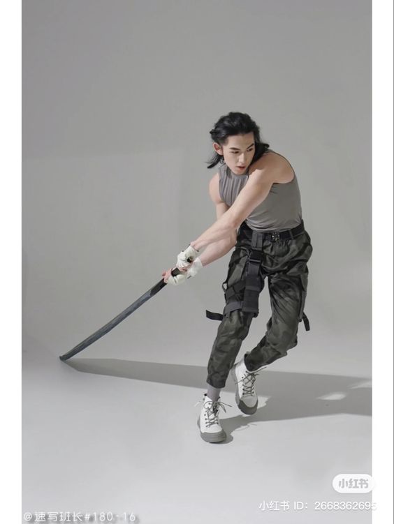 a man in a grey tank top and green cargo pants strikes a dynamic pose with a katana sword in a studio setting. his hair is long and pulled back, and he wears white sneakers and fingerless gloves. the image is framed with a white border and features chinese characters and numbers at the bottom right corner.