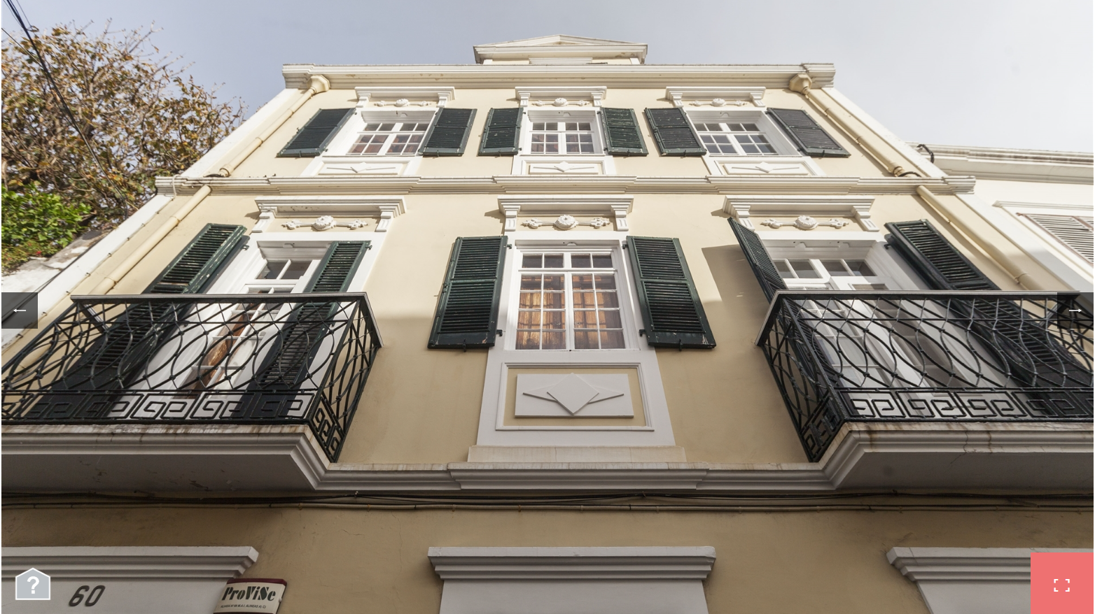 a low angle view of an old building with intricate details. the building has balconies with ornate wrought iron railings. the windows are also ornate and have shutters. the building is painted a pale yellow and the windows and balcony railings are painted black. the building appears to be in the historic district of a european city.  there are two house numbers visible on the building, '60' and '32'.