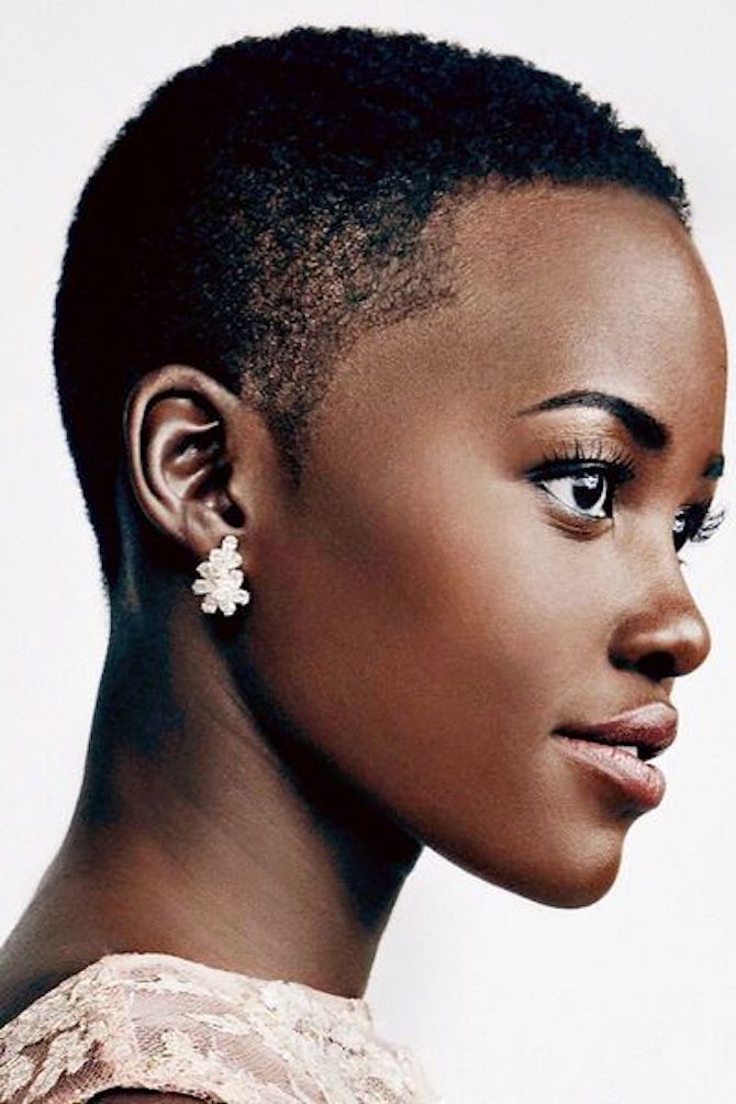 closeup portrait of a beautiful black woman with short hair, wearing earrings and looking away from the camera. she has on makeup and her hair is styled in a short, neat cut. the woman appears to be looking thoughtful or serious. the background is a plain white, which helps to focus attention on the woman's face and hair.