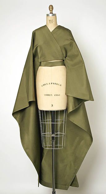 a green silk dress draped on a dress form. the dress has a simple, flowing design with a long, flowing skirt and a wraparound bodice. the dress is made of a lightweight silk fabric that drapes beautifully. the dress form is a standard size and shape, and it is positioned in the center of the image. the background is a plain white wall. the lighting is soft and diffused, creating a subtle contrast between the dress and the background.
